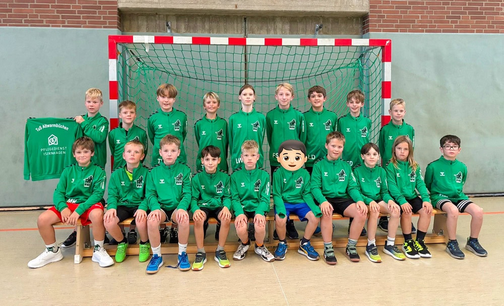 Junges Handballteam mit grünen Trainingsanzüge, gesponsort vom Pflegedienst Isernhagen sitzen auf einer Bank vor dem Tor.